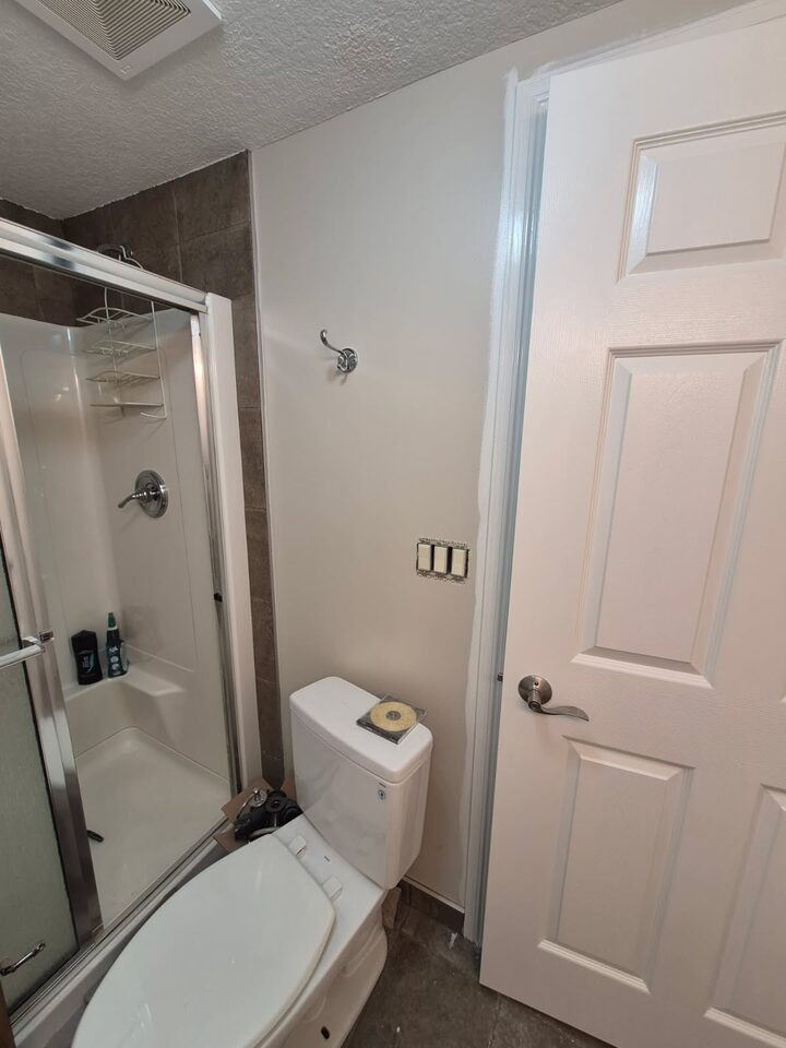 Before photo of the shower and toilet wall in a Chinook Park Calgary bathroom before peel-and-stick wallpaper installation