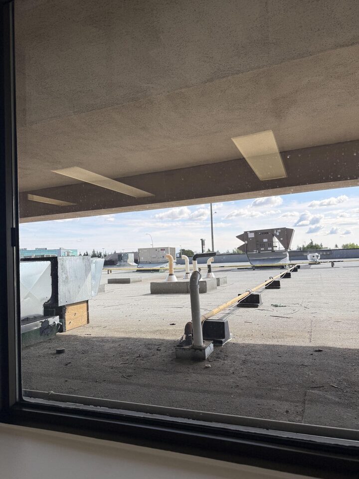 Clear second-floor office window before privacy film, looking straight onto the neighbouring flat roof and HVAC units, Centre 89 on Macleod Trail, Haysboro, SW Calgary