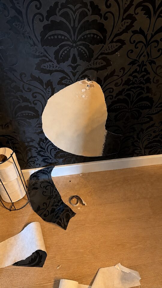Accidental damage to black damask wallpaper in a Heritage Pointe powder room before repair