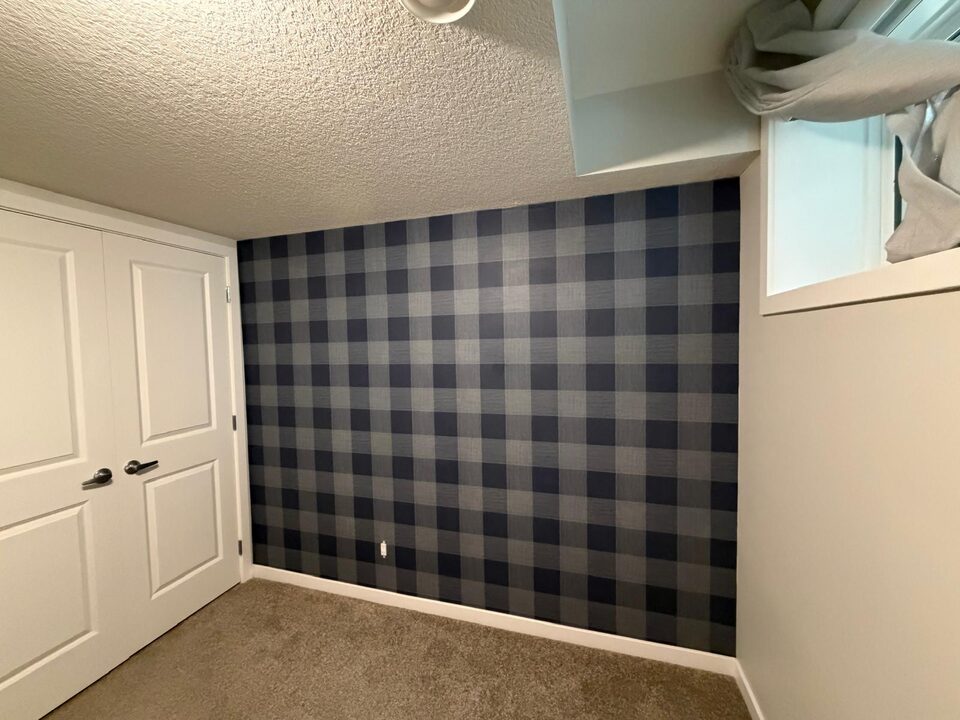 Buffalo check plaid wallpaper feature wall beside white closet doors in a Legacy, SE Calgary basement bedroom