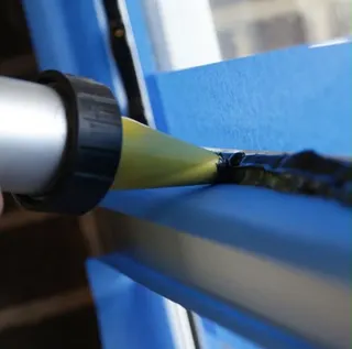 Illustrative close-up of black silicone being applied along a taped glass-to-frame edge