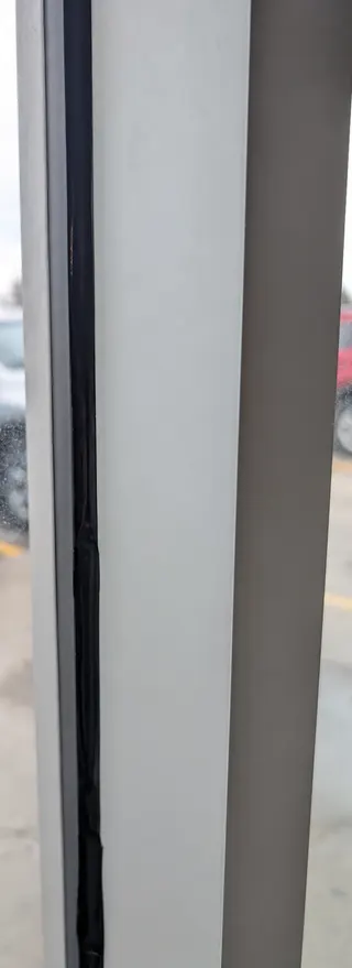 Close-up of a visible black silicone bead beside a light-coloured window frame