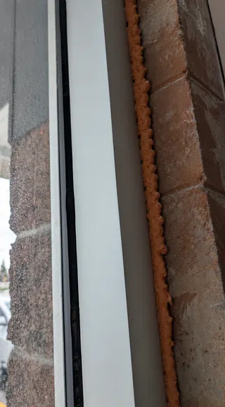 Black silicone bead at the glass edge next to a light-coloured frame and brick reveal
