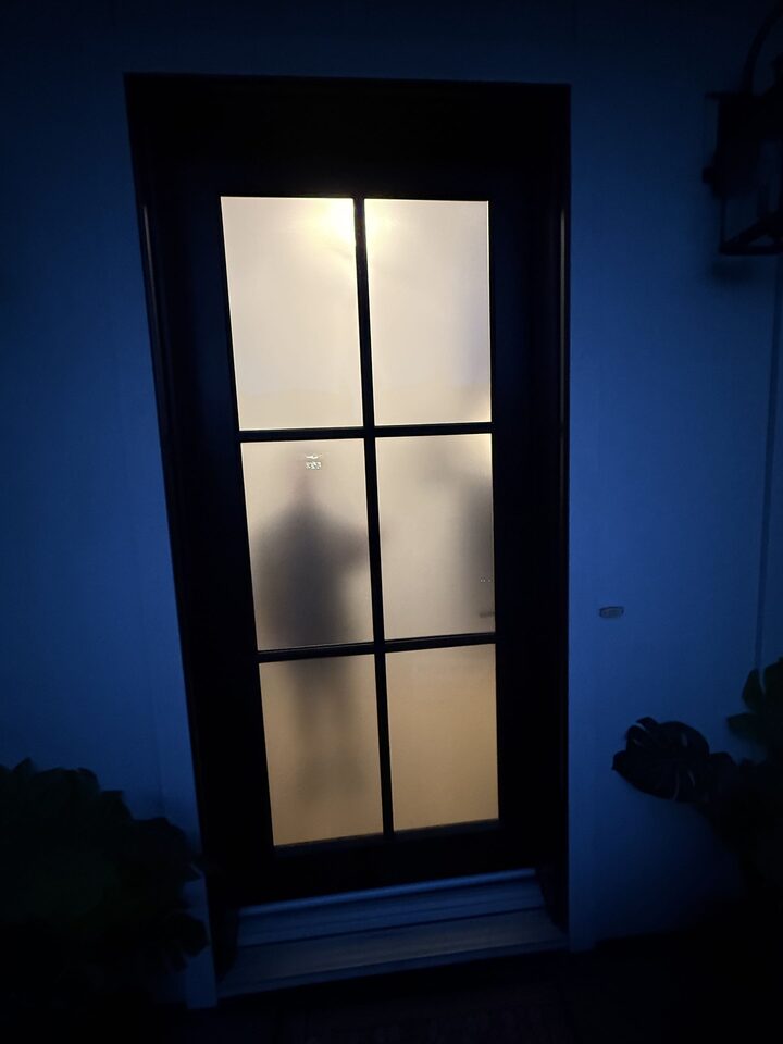 Altadore front door from outside at night with the hall lit, frosted film blurring the interior to a soft silhouette