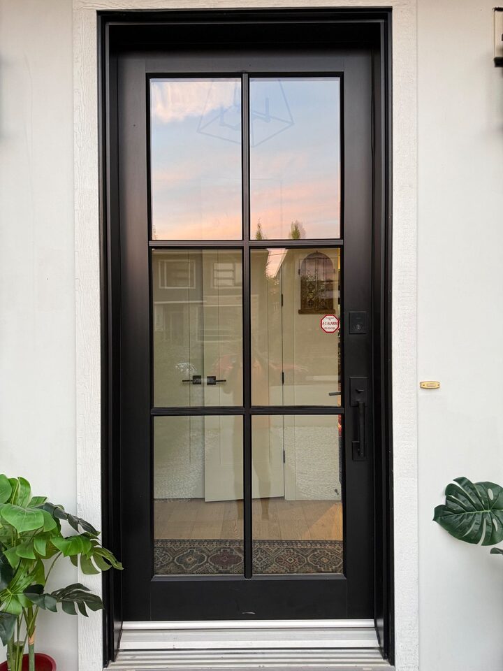 Black wooden front door in Altadore, Calgary before privacy film, with six clear glass panels showing the entry inside and reflecting the street