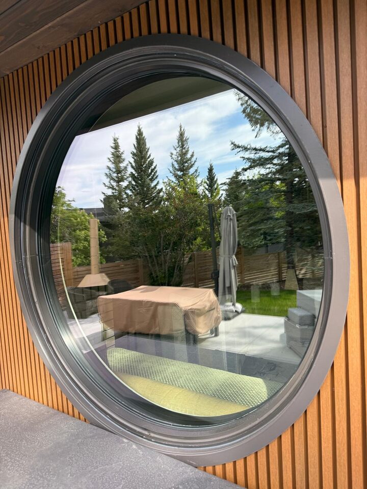 Before photo of the clear round feature window with a view straight through to the backyard, prior to solar window film in Britannia SW Calgary