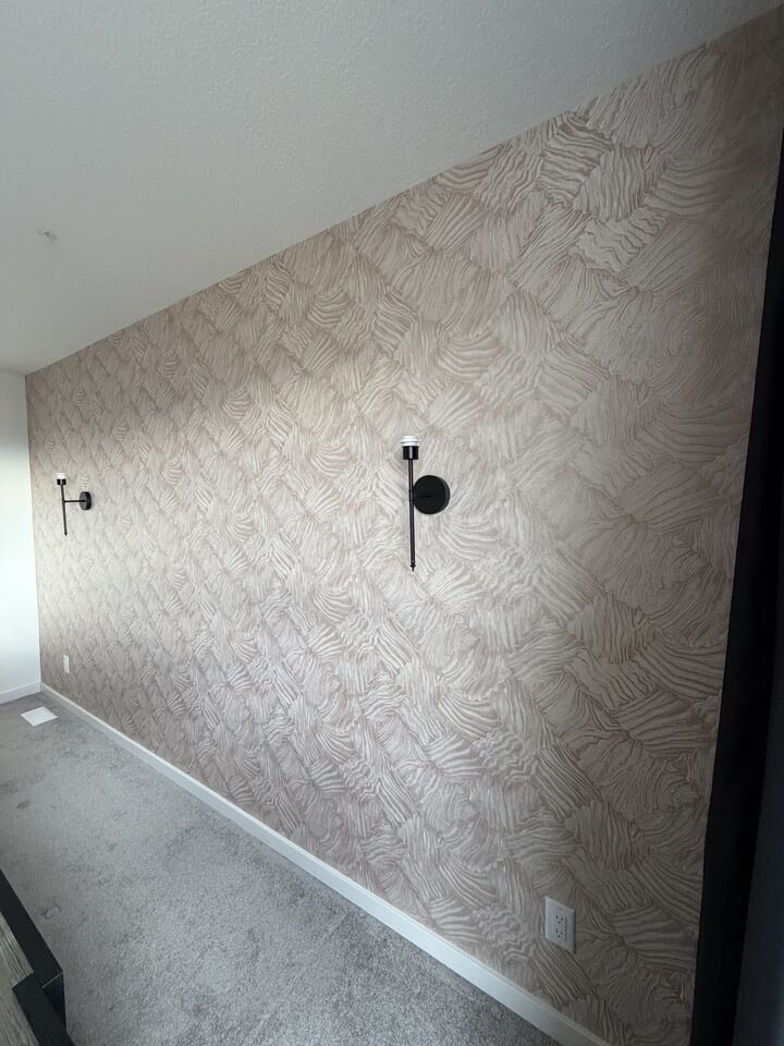 Angled view of rose-gold metallic textured wallpaper installed around black wall sconces in Cochrane