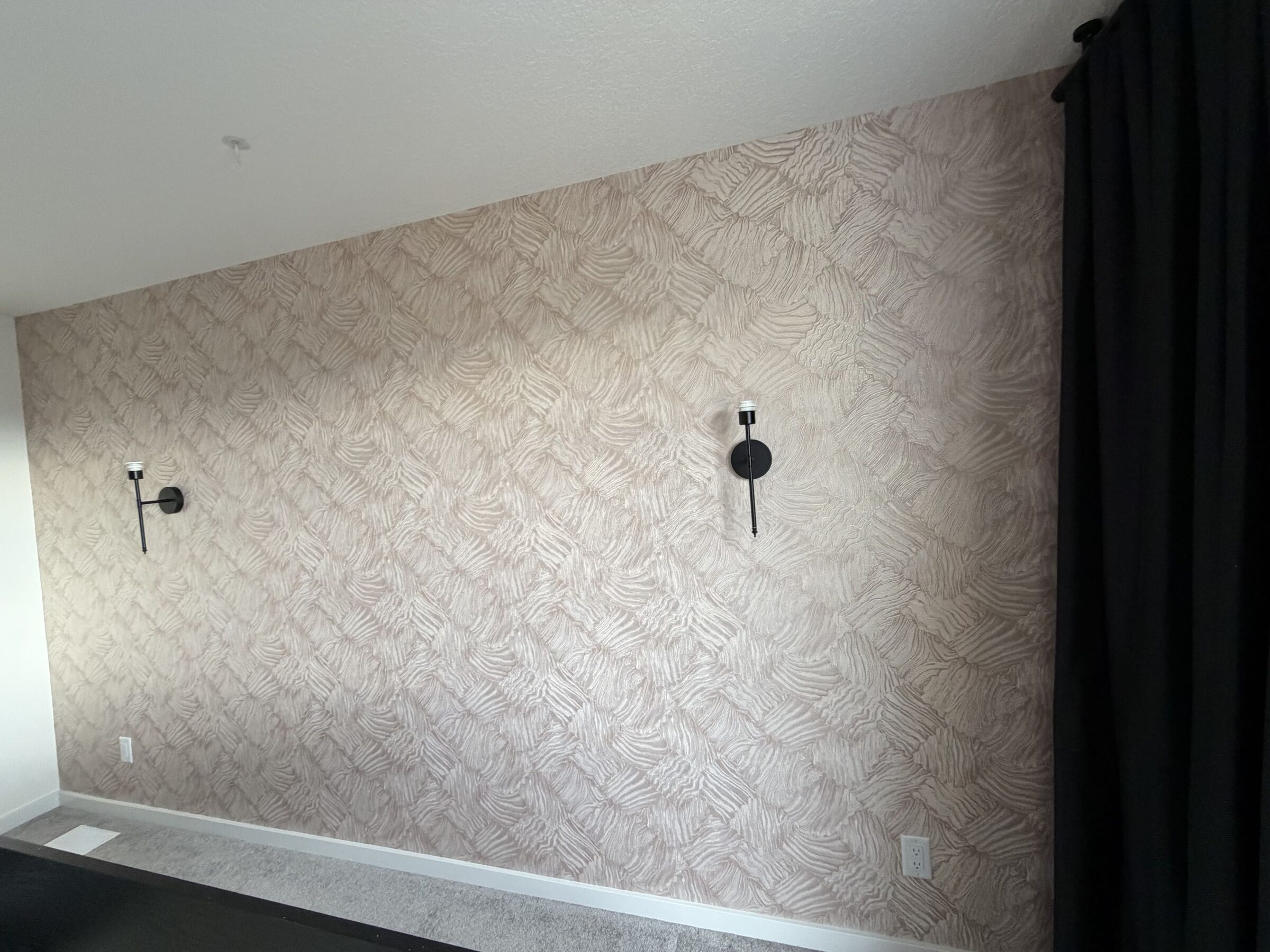 Finished rose-gold metallic textured wallpaper accent wall with black sconces in a Cochrane bedroom