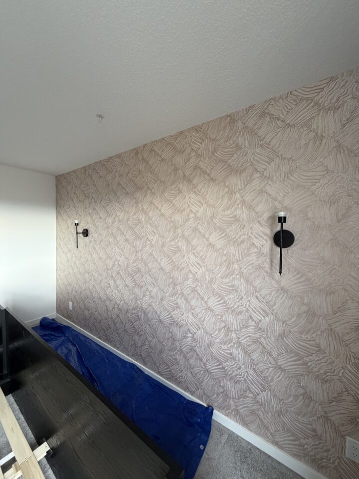Rose-gold textured wallpaper installation in progress with floor protection in a Cochrane bedroom