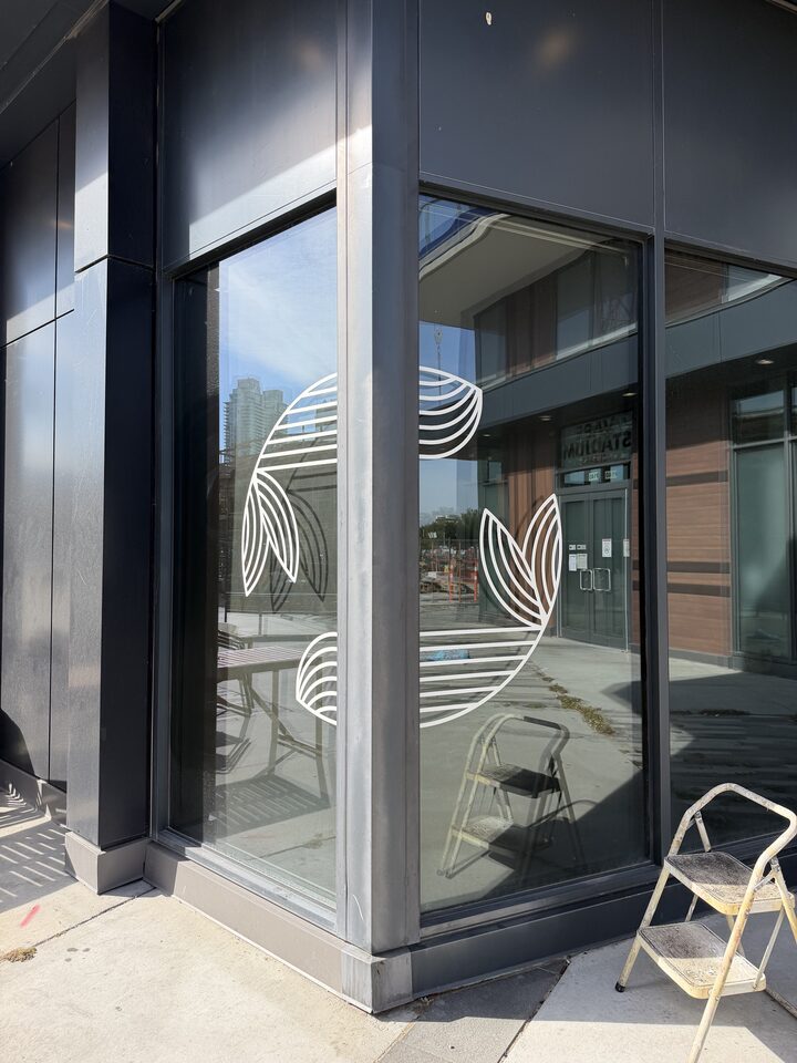 White cut-vinyl logo graphics on tinted corner storefront glass in East Village, Downtown Calgary