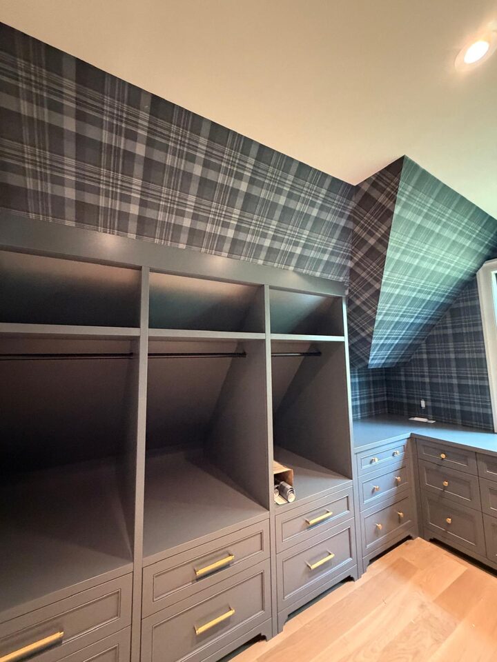 Plaid wallpaper pattern-matched down an angled dormer ceiling above gray built-in wardrobes in an Elbow Valley walk-in closet, Rocky View County