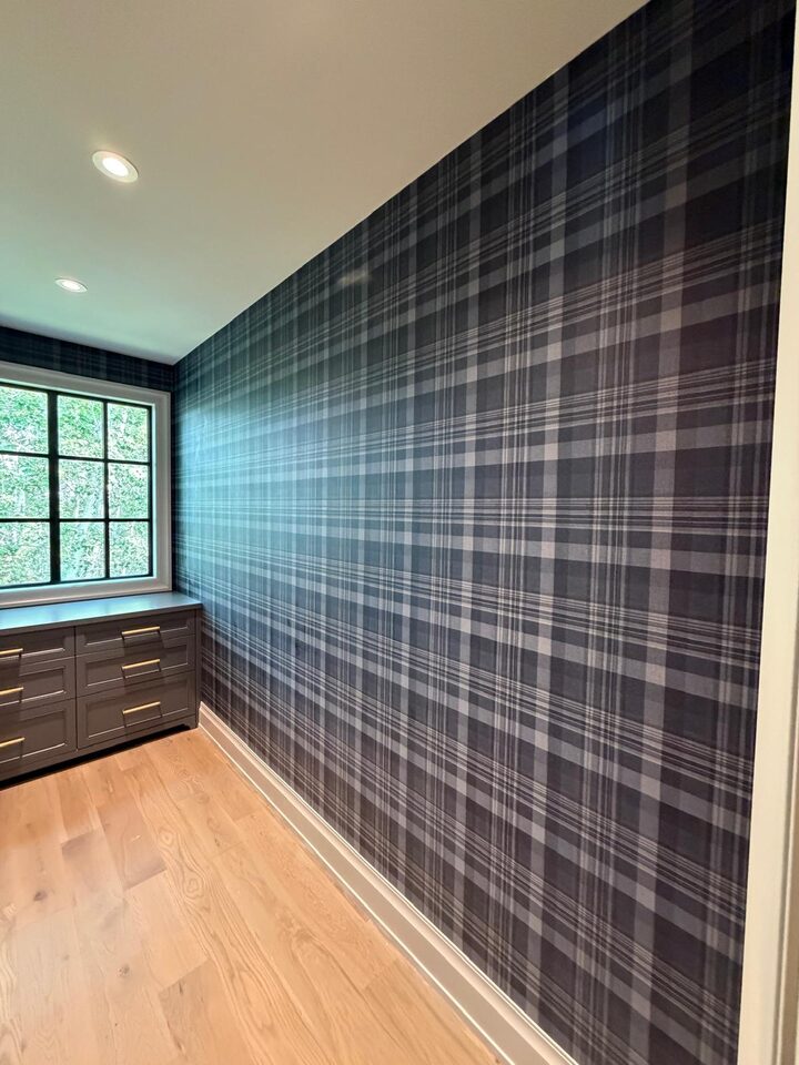 Charcoal tartan plaid wallpaper feature wall beside a forest-view window and built-in dresser in an Elbow Valley dressing room, west of Calgary