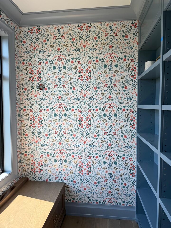 Mirror-repeat wildflower wallpaper wall beside blue built-in bookshelves in a new build home in Elbow Valley, Rocky View County