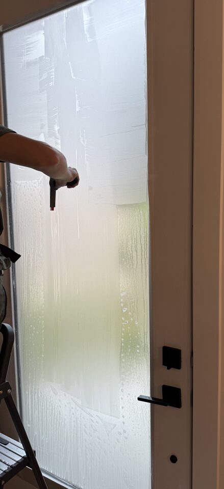 Installer squeegeeing Dusted Crystal frosted privacy film onto full-lite door glass during a Glenbrook SW Calgary installation