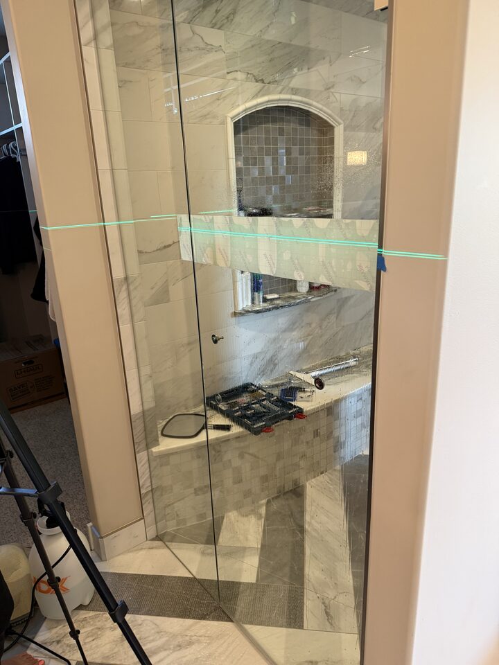 Clear glass shower enclosure with laser layout line before frosted privacy film installation in Heritage Pointe, south of Calgary