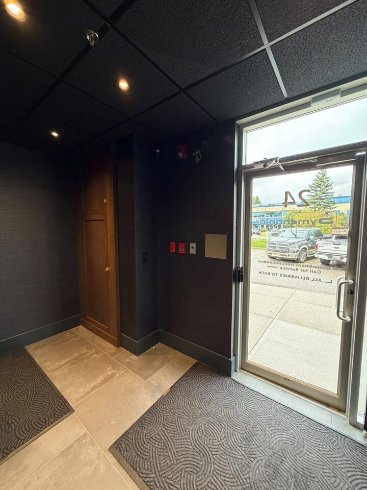 Entry vestibule with dark textured commercial wallcovering beside the glass front door, Highfield industrial office, SE Calgary