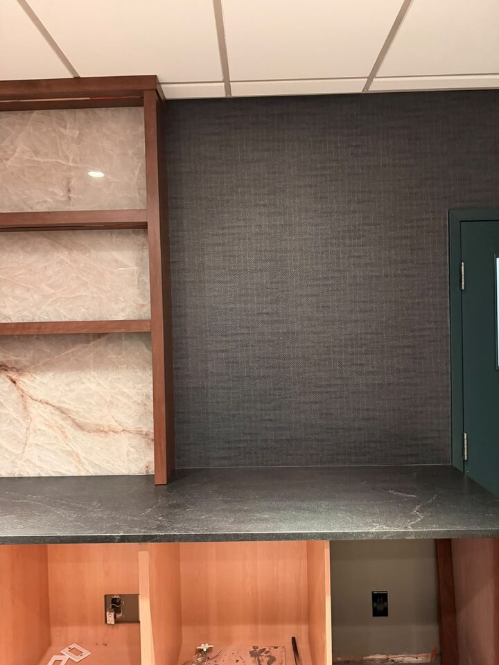 Charcoal commercial wallcovering set behind millwork shelving and a stone counter, Highfield office, SE Calgary