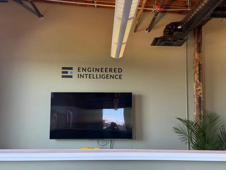 Custom logo wall graphic installed above a mounted TV on an office feature wall in Inglewood SE Calgary