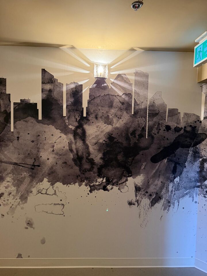 Close view of the black-and-white Calgary skyline mural wallcovering with ink-wash towers under a corridor sconce, downtown Calgary